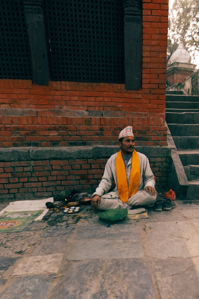A man in traditional attire sits by a brick wall, capturing cultural essence.