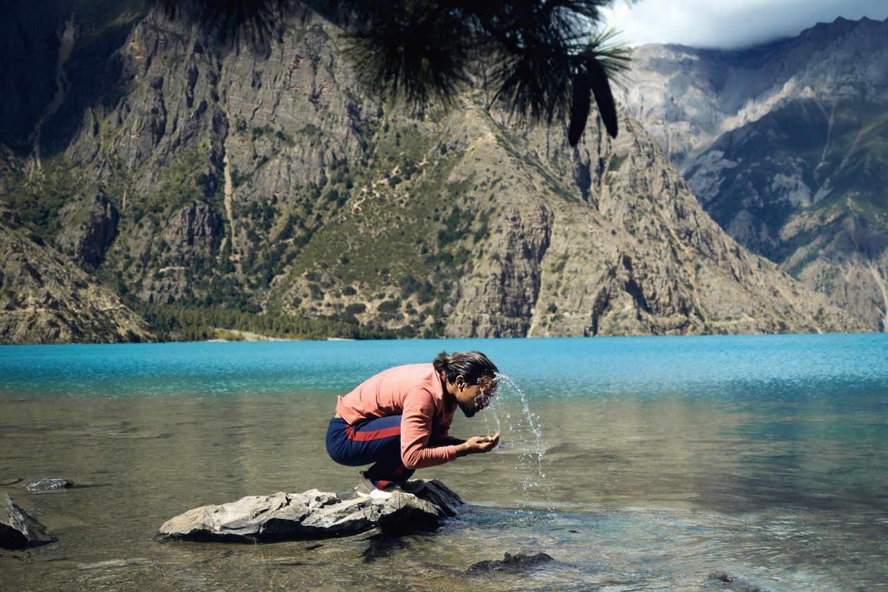 Man enjoying the pristine waters of Phoksundo Lake in Nepal, surrounded by towering mountains.