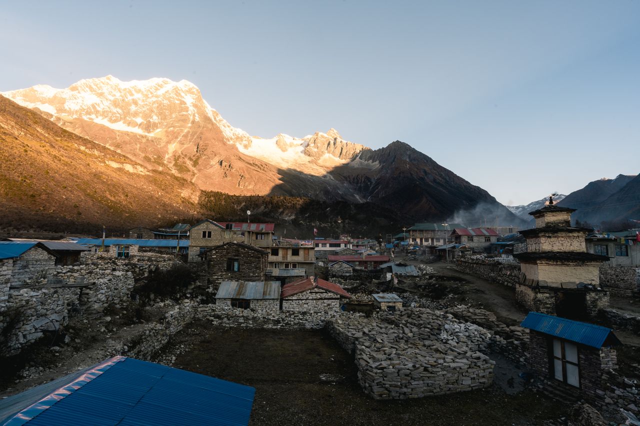 A serene Himalayan village with mountains at sunrise, showcasing rustic architecture in Nepal.