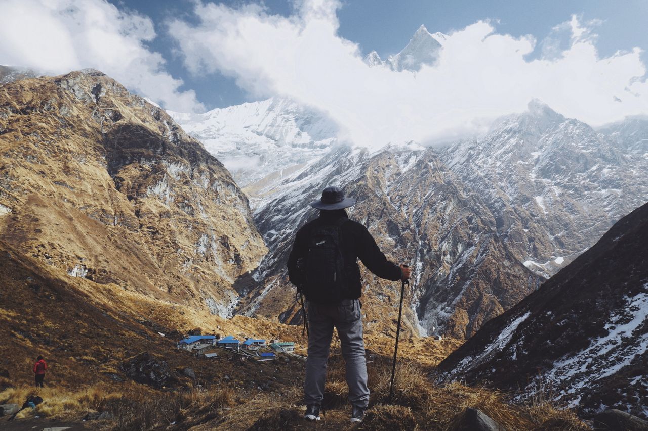 A lone hiker stands with trekking poles, admiring the breathtaking Himalayas in Nepal.